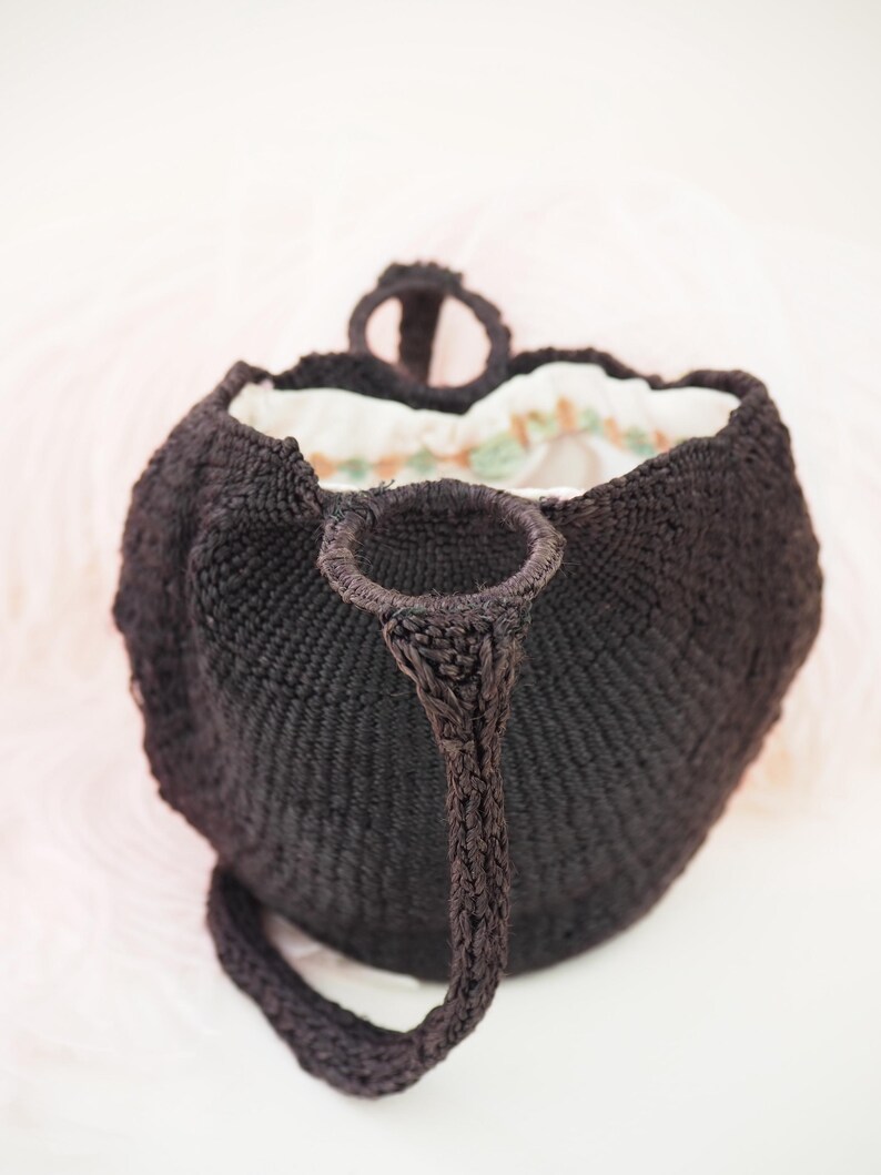 May include: A black woven tote bag with a single strap and a white and green floral lining.