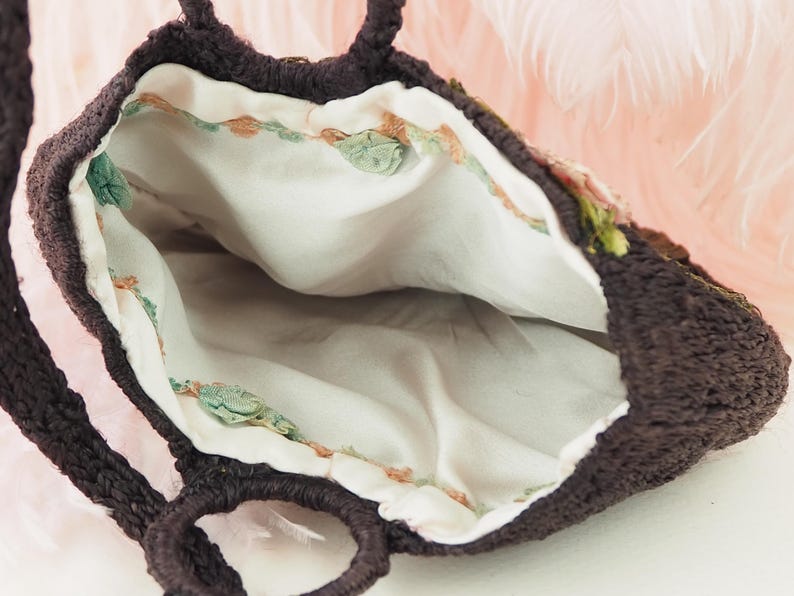 May include: A brown crocheted bag with a white fabric lining and floral embroidery. The bag has two handles.