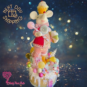May include: A whimsical Christmas tree topper featuring a pink mouse wearing a red and white candy-themed outfit. The mouse is holding a lollipop and a candy cane. The tree topper is decorated with candy canes, lollipops, and other candy-themed decorations.