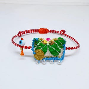 May include: Red and white string bracelet with a green and gold fabric charm, a blue and white beaded fringe, and a blue evil eye charm.