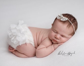 May include: A newborn baby girl sleeping on a white blanket, wearing a white lace diaper cover and a white lace headband.