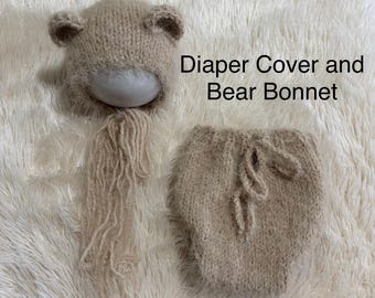 May include: A beige knitted bear bonnet with rounded ears and long fringe tassels, paired with a matching knitted diaper cover. The text Diaper Cover and Bear Bonnet is visible in the image. The items are made of a soft, textured yarn.