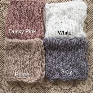 May include: Four knitted squares in different colors: dusky pink, white, beige, and grey. The squares are made of chunky yarn and have a textured, woven look.