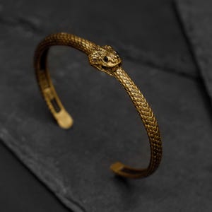 May include: A gold-toned snake cuff bracelet with a detailed snake head design.