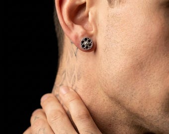 May include: A silver-toned ear plug with a circular design featuring multiple small holes and a central gold-colored accent. The jewelry is worn in the ear, showcasing a detailed, industrial aesthetic.