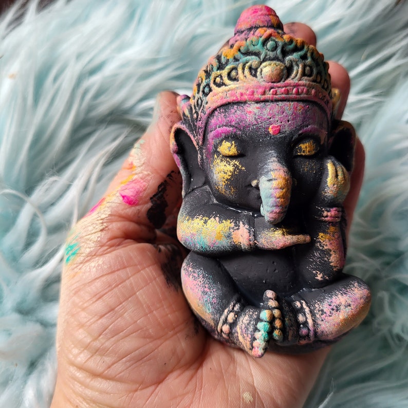 May include: A small, black, hand-painted figurine of the Hindu deity Ganesha. The figurine is decorated with colourful, abstract patterns and has a trunk raised to its mouth.