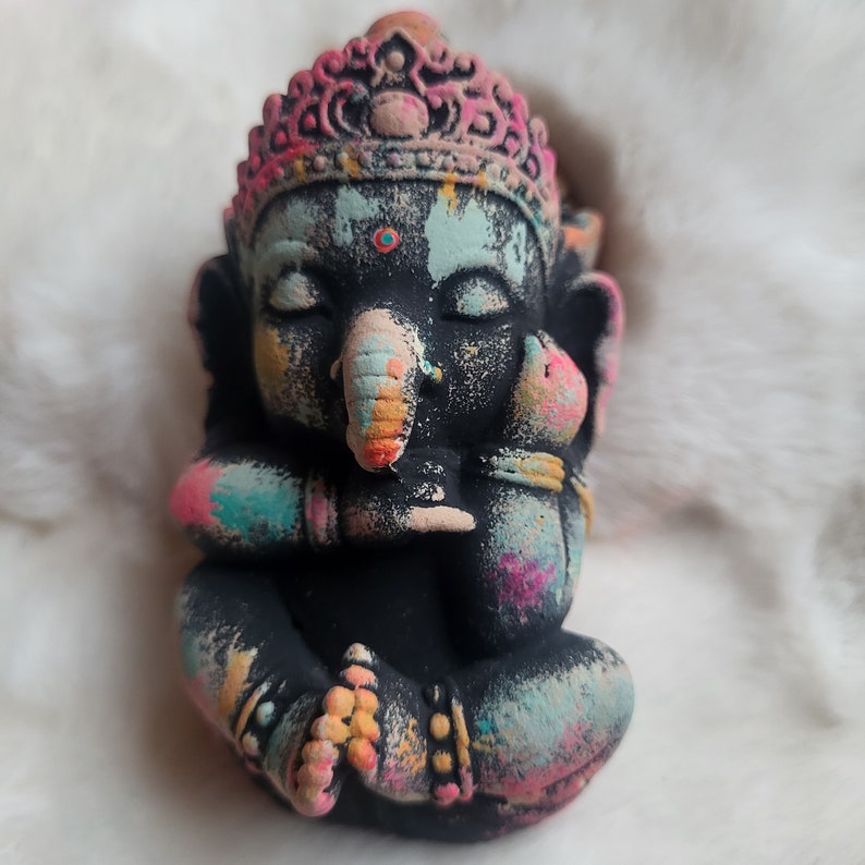 May include: A small black statue of Ganesha, the Hindu god of wisdom and prosperity. The statue is painted with colourful accents and has a crown on its head.