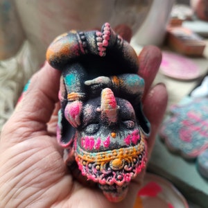 May include: A small, hand-painted figurine of a sleeping elephant wearing a pink and orange turban. The elephant is decorated with intricate details and colourful patterns.