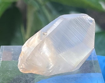 May include: A clear, faceted crystal point with a hexagonal shape. The crystal is resting on a clear acrylic display stand.