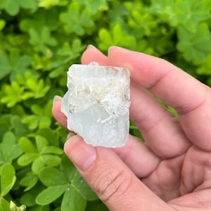 May include: A clear, light blue aquamarine crystal with a rough, natural texture. The crystal has a rectangular shape and is approximately 2 inches in length.