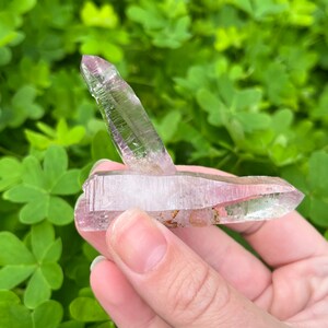 May include: A double-terminated amethyst crystal with a light pink hue and clear sections. The crystal is pointed at both ends and has a natural, raw appearance.