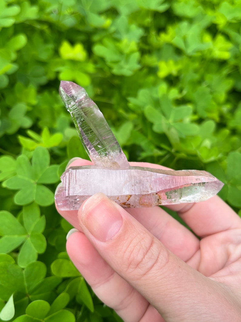 May include: A double-terminated amethyst crystal with a light pink hue and clear sections. The crystal is pointed at both ends and has a natural, raw appearance.
