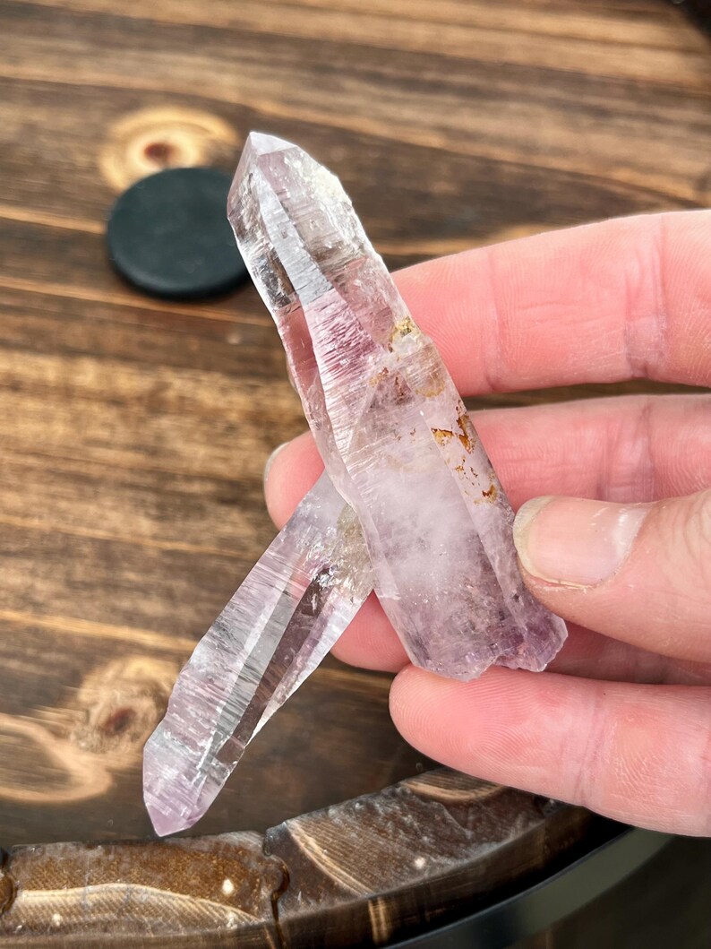 May include: Two clear quartz crystal points with a light purple hue. The crystals are pointed at the top and have a natural, rough texture.