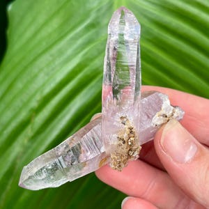 May include: Two clear quartz crystals with a purple hue, one is larger than the other, and both have a natural, raw look.