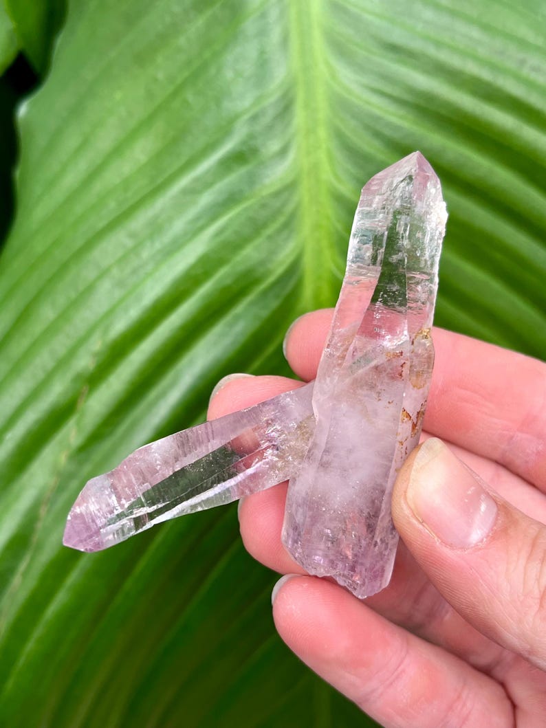 May include: Two clear quartz crystals with a light purple hue. The crystals are double terminated and have a natural, raw appearance.