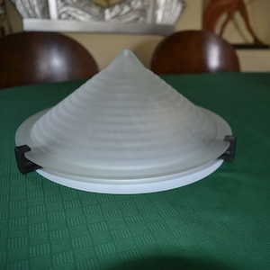 May include: A white frosted glass lampshade with a conical shape and a ridged design. The lampshade is attached to a black metal base.