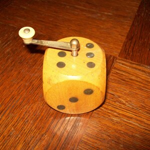 Könnte beinhalten: Ein hölzerner Pfeffermühle in Form eines Würfels mit schwarzen Punkten. Die Mühle hat einen kleinen, weißen Knopf an der Seite.