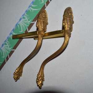 Könnte beinhalten: Zwei goldfarbene dekorative Türklinken mit verzierten Blumendesigns und einer gesichtsartigen Figur oben.