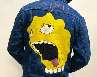 Könnte beinhalten: Eine blaue Jeansjacke mit einem gelben Comic-Charakter, der auf den Rücken gemalt ist. Der Charakter hat einen großen Mund und schreit "MAMA!" in rosa Buchstaben.