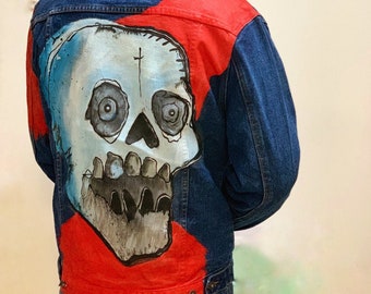 Könnte beinhalten: Eine blaue Jeansjacke mit einem roten und weißen Totenkopf, der auf den Rücken gemalt ist. Der Totenkopf ist realistisch gemalt mit Details wie Zähnen und Augen.