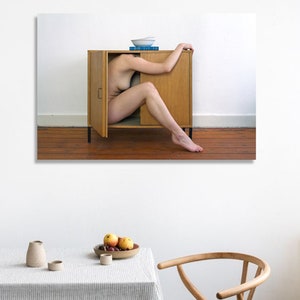 Puede incluir: Una fotograf&iacute;a muestra el cuerpo de una persona parcialmente dentro de un armario de madera con la puerta abierta. El armario est&aacute; contra una pared blanca y un suelo de madera. Un cuenco y libros est&aacute;n encima del armario. Una mesa con un mantel a rayas y fruta est&aacute; en primer plano.