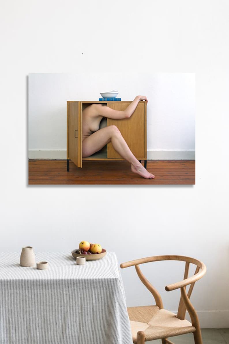 Puede incluir: Una fotograf&iacute;a muestra el cuerpo de una persona parcialmente dentro de un armario de madera con la puerta abierta. El armario est&aacute; contra una pared blanca y un suelo de madera. Un cuenco y libros est&aacute;n encima del armario. Una mesa con un mantel a rayas y fruta est&aacute; en primer plano.