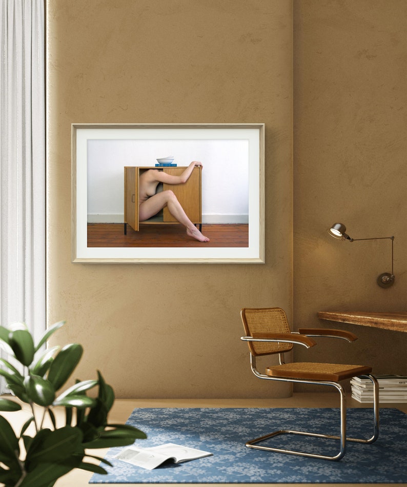 Puede incluir: Fotograf&iacute;a enmarcada de una persona dentro de un armario de madera abierto. Un cuenco y libros encima. La habitaci&oacute;n tiene una alfombra azul, una silla y un escritorio, todo sobre una pared beige.