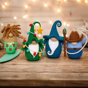 May include: Four crocheted gnomes in various outfits. One gnome is a surfer, another is a Christmas tree, a third is a wizard, and the last is a cowboy. The gnomes are on a wooden surface with a blurred background of lights.