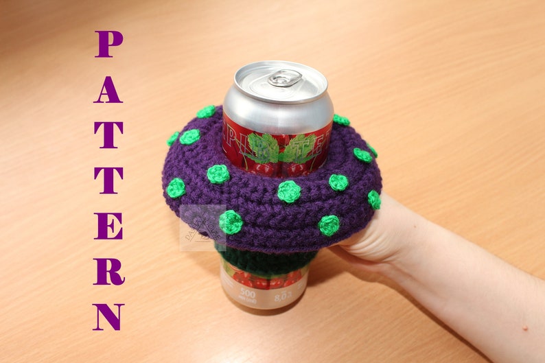 May include: A purple crocheted drink cosy with small green circular accents, featuring a wide brim that encircles a 500 ml aluminium beverage can. The word PATTERN is printed vertically in purple letters on the left side of the image.