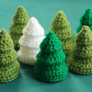 Puede incluir: Una colección de nueve árboles de Navidad de ganchillo en verde y blanco. Los árboles están dispuestos en semicírculo sobre una superficie verde.
