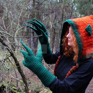 May include: A crochet set featuring a bright orange hooded cowl with dark green trim and pointed ear-like accents, paired with long dark green gloves that have elongated, claw-like fingers. The word PATTERN is printed vertically in white on the left.
