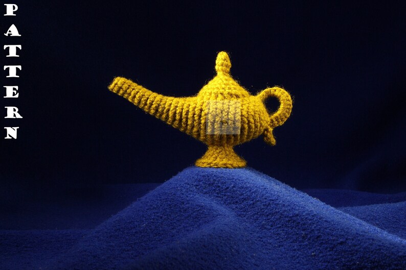 K&ouml;nnte beinhalten: Eine handgefertigte, goldgelbe H&auml;kellampe, die an eine Wunderlampe erinnert, steht auf einer blauen, strukturierten Oberfl&auml;che. Die Lampe hat einen gebogenen Ausguss, einen Griff und eine dekorative Oberseite. Das Wort "PATTERN" wird links vertikal angezeigt.