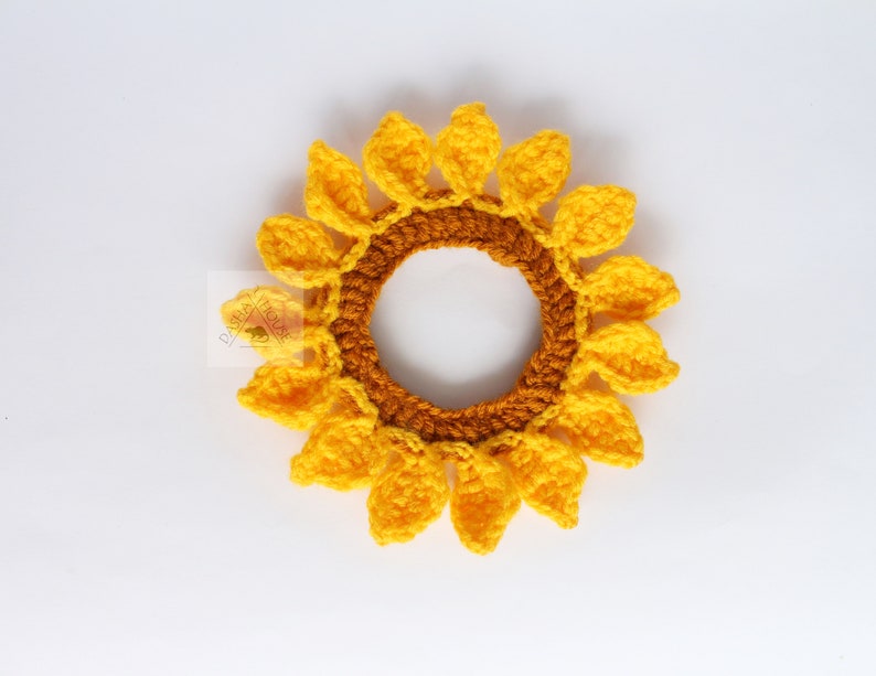 May include: A handmade crochet sunflower hair tie. The hair accessory features a bright yellow flower with a brown center and yellow petals. The sunflower is a cheerful and summery accessory.