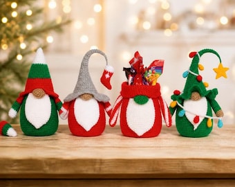 Puede incluir: Cuatro figuras de gnomos de ganchillo hechas a mano en colores festivos. Los gnomos tienen cuerpos rojos, verdes y blancos, con varios sombreros y elementos decorativos. Un gnomo sostiene un calcetín pequeño y otro está decorado con luces navideñas.