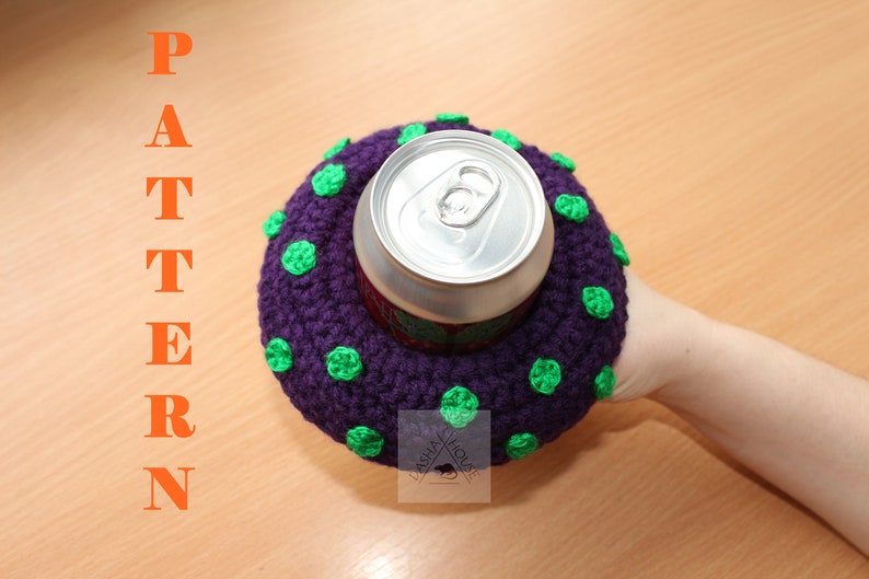 May include: A purple crocheted drink cosy with small green polka dots surrounding a silver aluminium beverage can. The word PATTERN is printed in orange vertically on the left side, and a logo with the text LASHA HOUSE is visible.