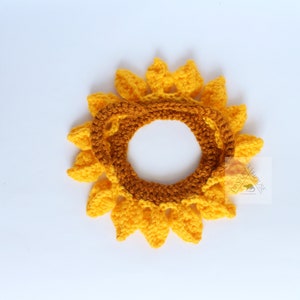 May include: A handmade crochet sunflower, featuring bright yellow petals and a brown center. The sunflower is designed to be worn as a headband or accessory. The craftwork is displayed on a white background.