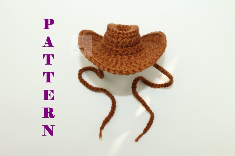Puede incluir: Un sombrero de vaquero marr&oacute;n tejido a ganchillo con ala ancha y cord&oacute;n. La palabra "PATTERN" se muestra verticalmente en letras moradas en el lado izquierdo de la imagen. El sombrero est&aacute; hecho de hilo texturizado.