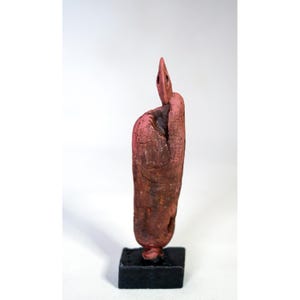 Peut inclure: Sculpture abstraite de couleur brun rougeâtre, montée sur une petite base carrée noire. La sculpture présente une surface texturée et un sommet pointu, ressemblant à un doigt stylisé ou à une forme naturelle.