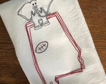 Op de afbeelding: Witte keukendoek met een rode geborduurde omtrek van de staat Alabama, een bruine voetbal en een grijze olifant.