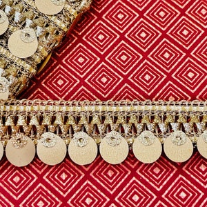 May include: Gold and beige trim with a fringe and round sequins. The trim is on a red background with a diamond pattern.