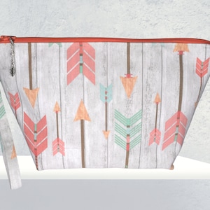 May include: A white zippered pouch with a woodgrain pattern and colorful arrows. The pouch has a coral zipper and a coral and white strap.