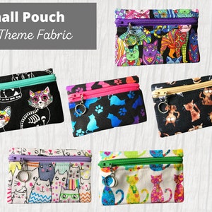 May include: Six small zippered pouches with cat-themed fabric. The pouches are in various colors and patterns, including black with a skull and crossbones, blue with paw prints, black with cats, white with colorful cats, and white with colorful cats. Each pouch has a silver key ring attached to the zipper.