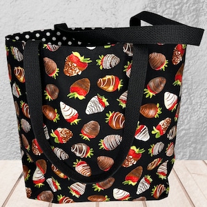 May include: A black tote bag with a white polka dot lining. The bag features a repeating pattern of chocolate-covered strawberries on a black background.