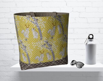 May include: A yellow tote bag with a white cat and antlers pattern. The bag has brown straps and a brown and gray checkered bottom.