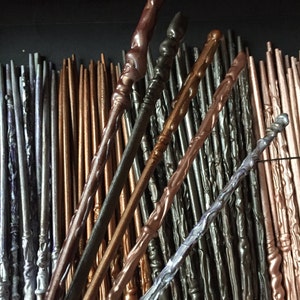 May include: A collection of wooden wands in various shades of brown, silver, and black. The wands are arranged in a random pattern, with some overlapping. The wands are all about the same length and have a slightly pointed tip.