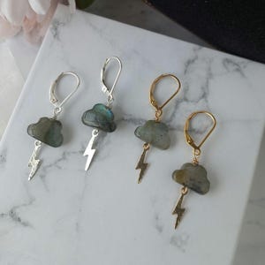 Peut inclure: Trois paires de boucles d'oreilles avec un design nuage et éclair. Les nuages sont en labradorite et les éclairs sont en argent et en or.