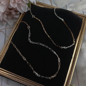 May include: Three delicate necklaces with small silver beads on a black velvet background. The necklaces are made of gold and silver chain links.