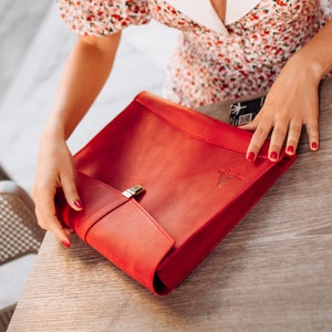 Könnte beinhalten: Ein rotes Lederportfolio mit einem goldenen Verschluss und einem geprägten Logo auf der Vorderseite.