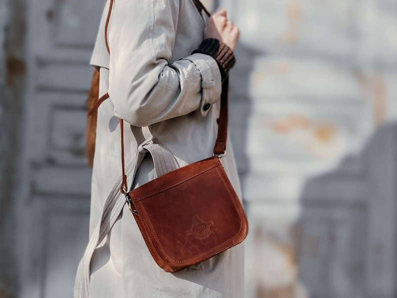 May include: A brown leather crossbody bag with a flap closure and a silver buckle. The bag has a long strap and is worn over the shoulder.