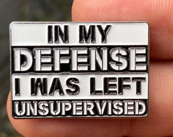 Puede incluir: Un pin de esmalte blanco y negro con el texto "In My Defense I Was Left Unsupervised".